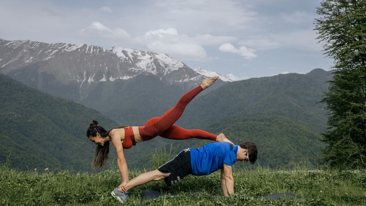 Couple doing yoga exercises outdoors with a breathtaking mountain view.